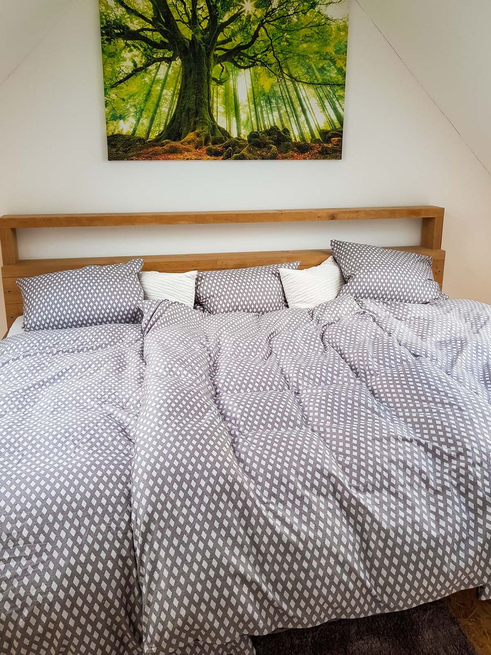 Doppelbett mit hellem Holzkopfteil, darüber ein großformatiges Waldbild