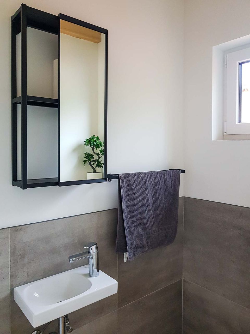 Badezimmer mit Waschbecken, Spiegelschrank und grau gefliester Wand