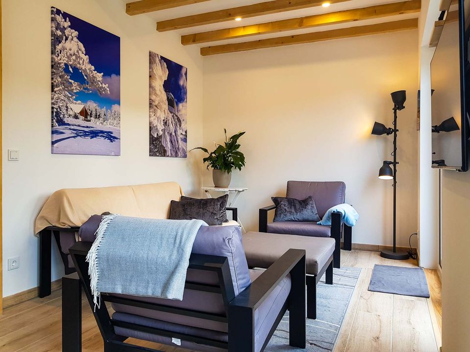 Wohnzimmer mit Couch, Sesseln und Winterbildern an der Wand