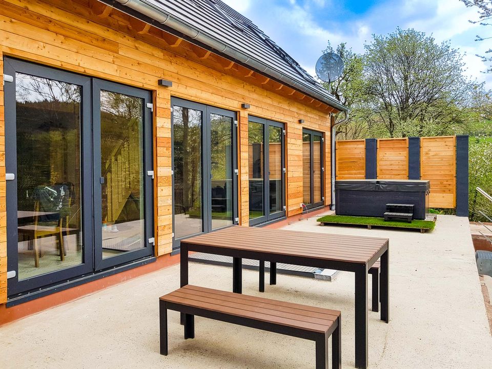 Sonnige Terrasse mit Sitzgruppe und Außenwhirlpool vor der Glasfront des Chalets