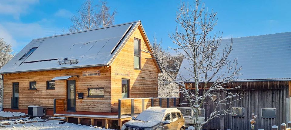Das Chalet Wasserkuppe im Winter: Holzfassade und schneebedecktes Dach vor blauem Himmel
