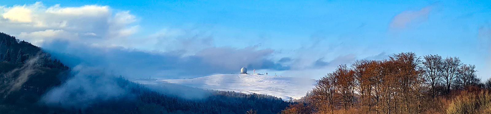 Verschneite Wasserkuppe mit Radom über einer Nebeldecke im Winter